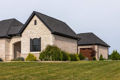 Glen-Gery | Limestone Cashmere building stone veneer on exterior of home with brick, black window shutters, and portico garage